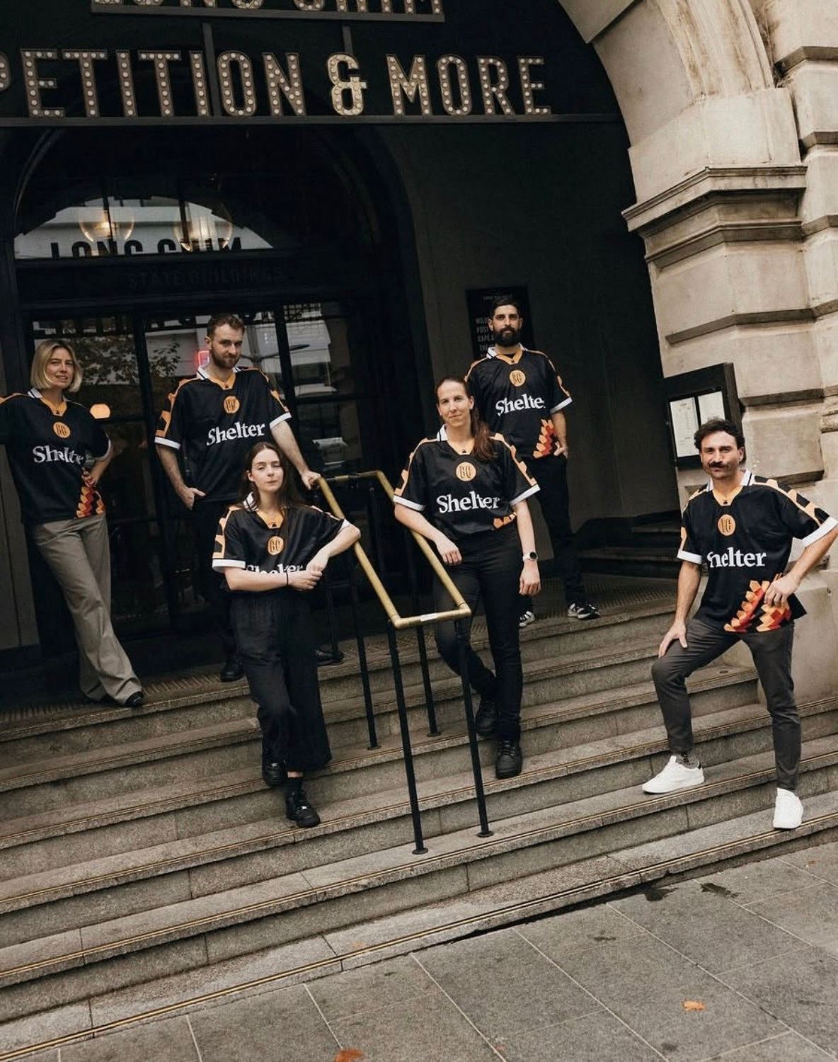 Team of six wearing matching custom screen printed jerseys produced for Shelter and Petition and More, on the steps of a Perth heritage building