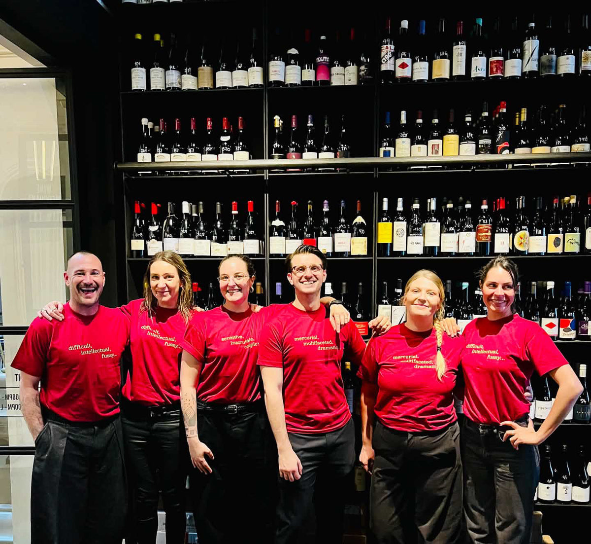 Wine Merchant team of six in matching red printed tees in front of the wine wall at State Building Perth